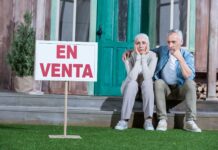 Fotografía de una pareja sentada a la puerta de su casa, con gesto de desánimo al no conseguir venderla.