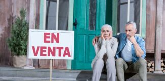 Fotografía de una pareja sentada a la puerta de su casa, con gesto de desánimo al no conseguir venderla.