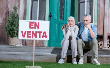 Fotografía de una pareja sentada a la puerta de su casa, con gesto de desánimo al no conseguir venderla.